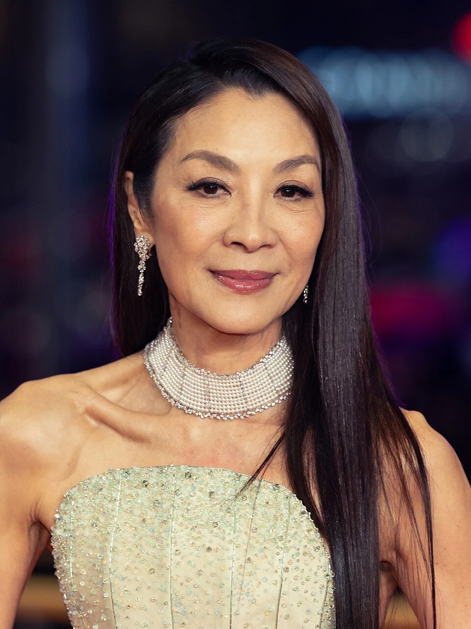 Michelle Yeoh posing on the red carpet in a formal strapless gown and jeweled necklace.