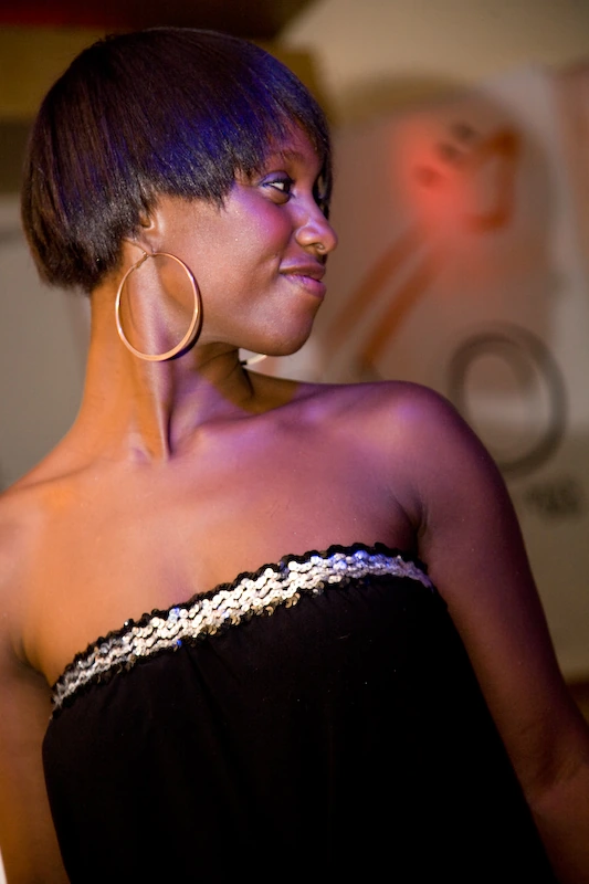 Michelle Gayle posing at an event, shown in profile wearing a black strapless top and large hoop earrings.