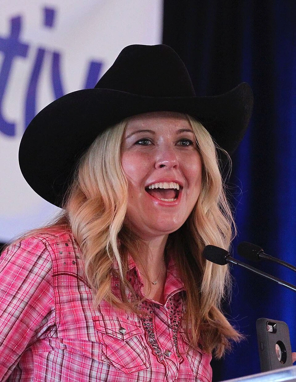 Michelle Rempel Garner speaking at a podium, wearing a black cowboy hat and pink plaid shirt.